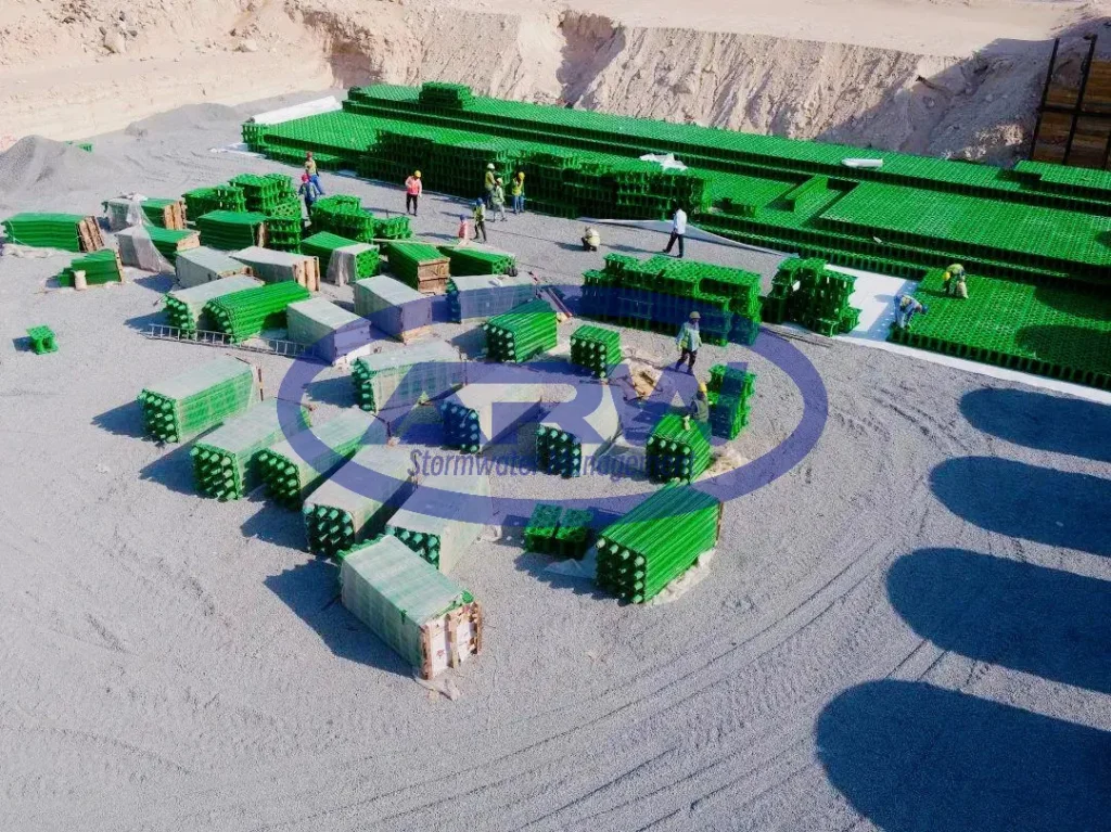 Crew installing green geocellular crates for an underground stormwater infiltration bed on a compacted granular base at a Middle East jobsite.